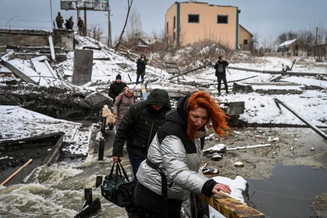 Civilians cross a river on a blown up bridge on Kyiv's northern front on March 1, 2022